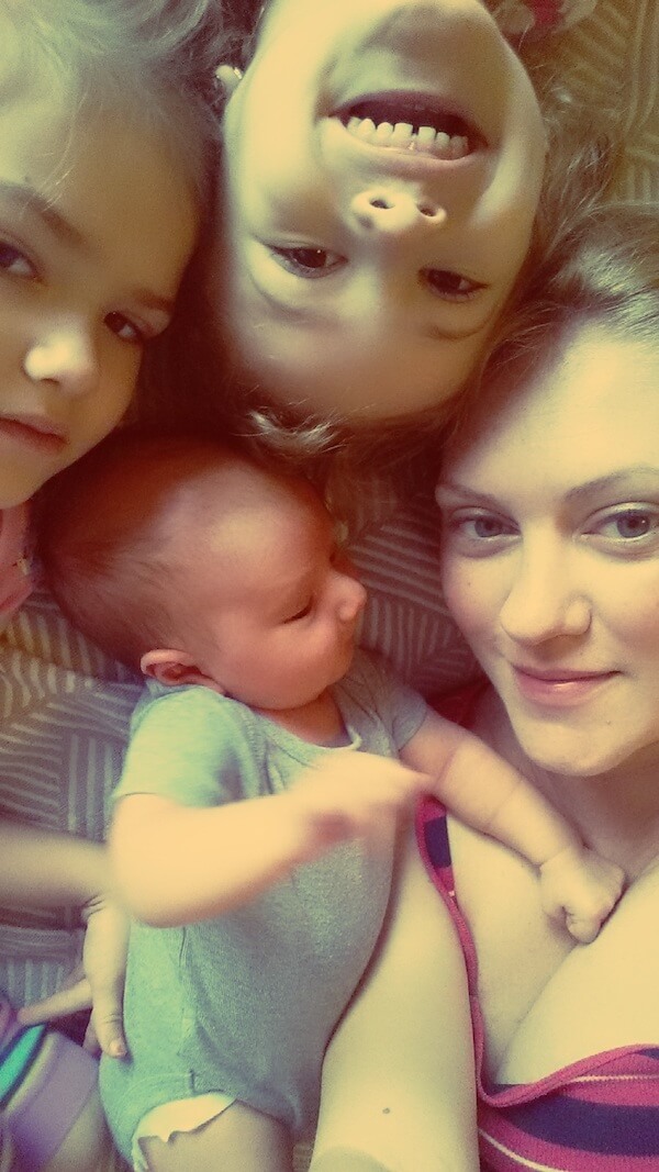 Children smiling, while laying down close with newborn baby.