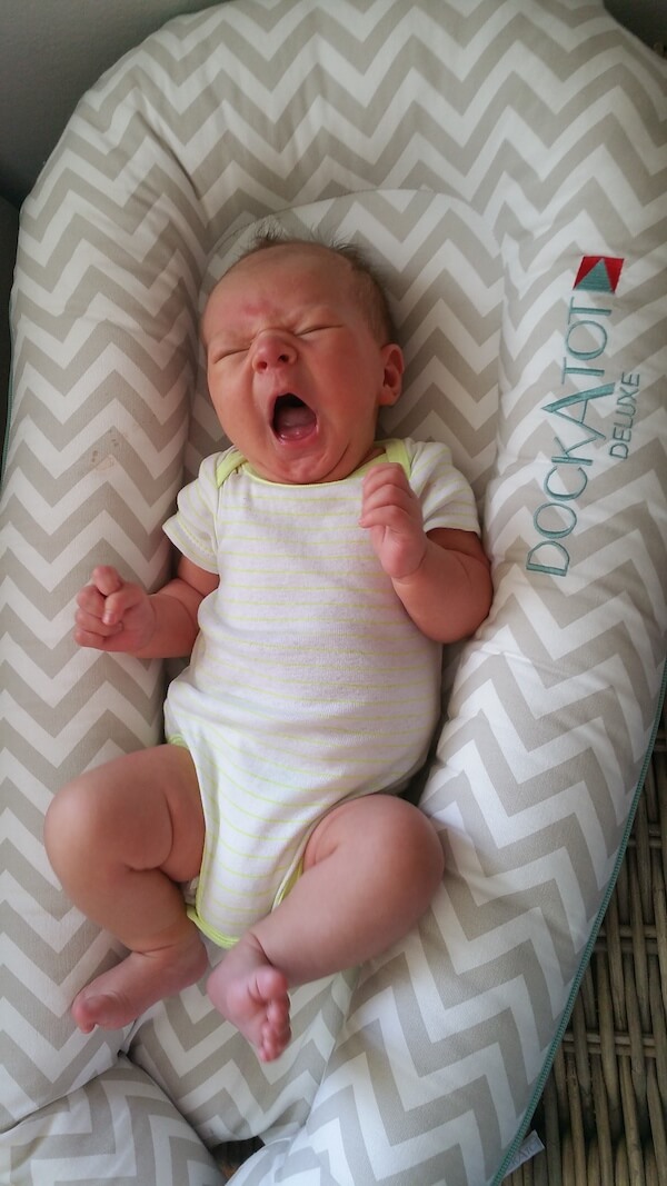 Children smiling, while laying down close with newborn baby.